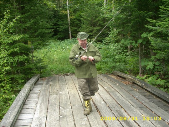 Photo of George Clark Stone walking across wilderness bridge with fishing pole